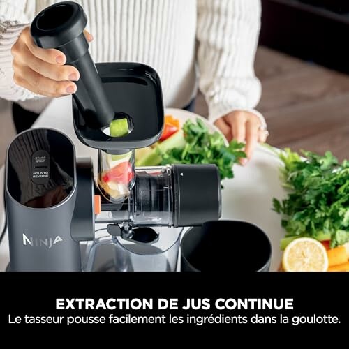 Personne utilisant un extracteur de jus Ninja avec des légumes et des fruits.